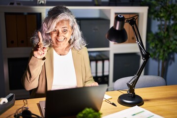 Canvas Print - Middle age woman with grey hair working using computer laptop late at night pointing finger up with successful idea. exited and happy. number one.