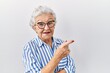 © Krakenimages.com - Senior woman with grey hair standing over white background with a big smile on face, pointing with hand and finger to the side looking at the camera.