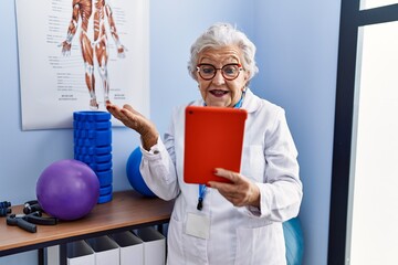 Wall Mural - Senior woman with grey hair working physiotherapy clinic doing video call celebrating achievement with happy smile and winner expression with raised hand