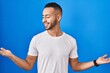 © Krakenimages.com - Young hispanic man standing over blue background smiling showing both hands open palms, presenting and advertising comparison and balance