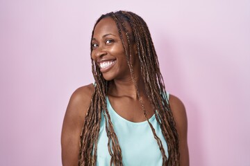 Wall Mural - African american woman standing over pink background looking away to side with smile on face, natural expression. laughing confident.