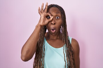 Sticker - African american woman standing over pink background doing ok gesture shocked with surprised face, eye looking through fingers. unbelieving expression.