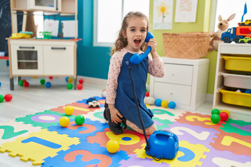 Poster - Adorable blonde girl playing with telephone toy sitting on floor at kindergarten