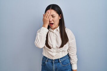 Poster - Young latin woman standing over blue background yawning tired covering half face, eye and mouth with hand. face hurts in pain.