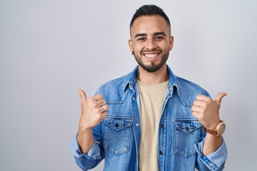 Poster - Young hispanic man standing over isolated background success sign doing positive gesture with hand, thumbs up smiling and happy. cheerful expression and winner gesture.