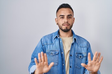 Sticker - Young hispanic man standing over isolated background moving away hands palms showing refusal and denial with afraid and disgusting expression. stop and forbidden.