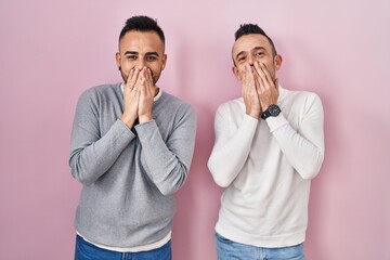 Canvas Print - Homosexual couple standing over pink background laughing and embarrassed giggle covering mouth with hands, gossip and scandal concept