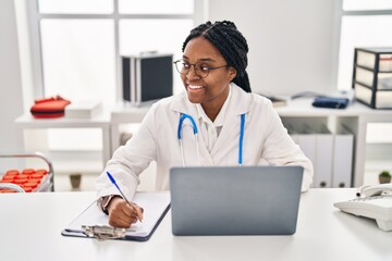 Poster - African american woman doctor using laptop writing medical report at clinic