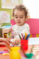 Poster - Adorable hispanic toddler student sitting on table drawing on paper at kindergarten