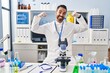 © Krakenimages.com - Young hispanic man with beard working at scientist laboratory showing arms muscles smiling proud. fitness concept.