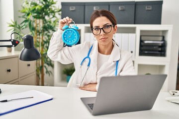 Wall Mural - Young brunette doctor woman holding alarm clock thinking attitude and sober expression looking self confident