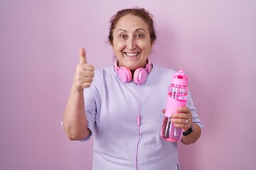 Sticker - Senior woman wearing sportswear and headphones doing happy thumbs up gesture with hand. approving expression looking at the camera showing success.