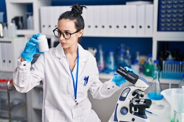 Sticker - Young caucasian woman scientist using microscope holding pills bottle at laboratory