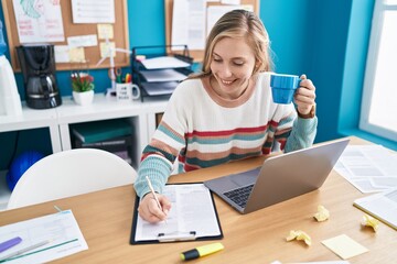 Canvas Print - Young blonde woman business worker drinking coffee writing on document at office