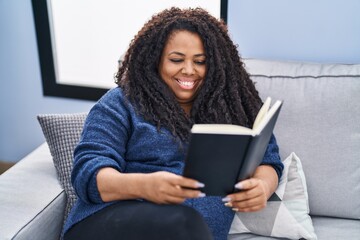 Canvas Print - African american woman reading book sitting on sofa at home