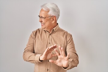 Poster - Hispanic senior man wearing glasses disgusted expression, displeased and fearful doing disgust face because aversion reaction. with hands raised