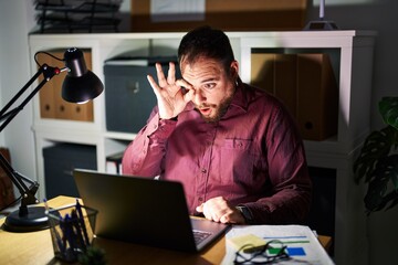 Canvas Print - Plus size hispanic man with beard working at the office at night doing ok gesture shocked with surprised face, eye looking through fingers. unbelieving expression.