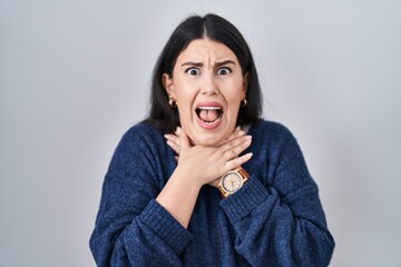 Wall Mural - Young brunette woman standing over isolated background shouting suffocate because painful strangle. health problem. asphyxiate and suicide concept.