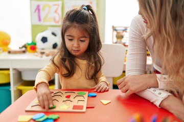 Poster - Teacher and toddler playing with maths puzzle game sitting on table at kindergarten