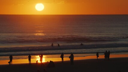 Wall Mural - silhouettes of people walking on sandy beach and surfers at the sunset background on the atlantic co
