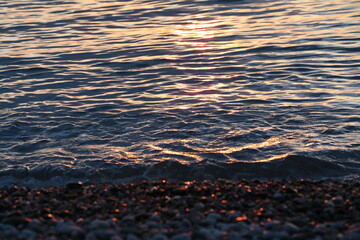 A wave rolls onto the beach at sunset with the reflection of sunlight on the surface of the water and the shore