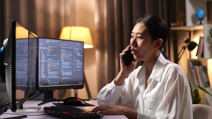 Asian Woman Programmer Talking On Smartphone While Creating Software Engineer Developing App, Program, Video Game On Desktop Computer At Home. Terminal With Coding Language 
