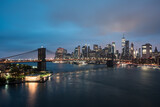 Fototapeta  - Skyline von New York in der Dämmerung mit Brooklyn Bridge und Lichtern am Fluss.
