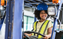 Little Girl Wearing Hard Hat, Driving Tractor In Factory, Smiling, Playing Alone As Worker With Happiness, Doing Activities On Weekend. Industry, Education Concept.