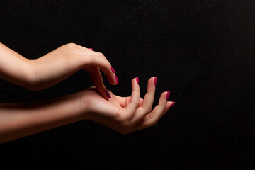 Wall Mural - Female hands with beautiful manicure - viva magenta, pink nails on dark black background. Nail, skin care concept