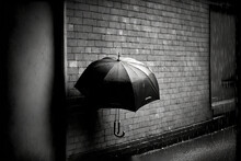  A Black And White Photo Of A Person Holding An Umbrella In The Rain On A Brick Wall In The City, With A Brick Wall Behind Them.  Generative Ai