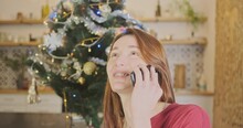 Young Girl Talking On Phone At Christmas. Portrait, Happiness, Face. Living Room, Indoors, Christmas Tree With Garland Of Light Bulbs.