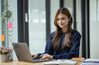 © SOMKID - Happy smiling young asian business woman using laptop sitting at desk in the office, Company worker woman.