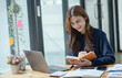 © SOMKID - Happy smiling young asian business woman paper notebook and laptop in the office, Company worker woman.
