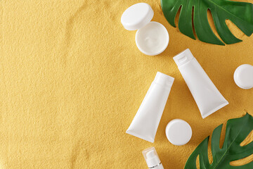 Wall Mural - Sunscreen cosmetic concept. Top view photo of white cosmetic tubes, cream jars and green tropical leaves on sandy background with empty space. Sun protection idea. Blank label for branding mockup.