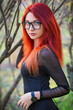 Attractive young girl with red hair, wearing glasses, posing near a tree