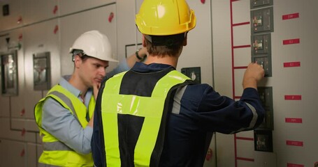 Wall Mural - Two electricians electrical engineers in protective uniform checking voltage control panel screen system at electrical cabinet for generate electricity of factory in manufacture industrial