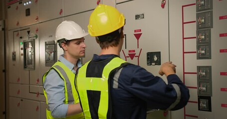 Wall Mural - Two electricians electrical engineers in protective uniform checking voltage control panel screen system at electrical cabinet for generate electricity of factory in manufacture industrial