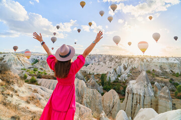 Girl traveler with open arms vacations beautiful destination in Goreme, Turkey. Fabulous Kapadokya with flying air balloons at sunrise, Anatolia