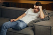© JJ Studio - Man falling asleep at home while watching TV. Lazy freelancer lying on sofa during working hours.