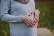A pregnant woman shows with her hand gestures a heart shape against the background of her belly.