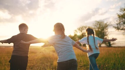 Wall Mural - kids run in the park at sunset. happy family children camp kid dream concept. a group of children run on the grass at sunset the rays of the sun silhouette. childhood dream fun teamwork concept