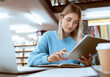 © J Maas/peopleimages.com - Education, university and woman in library with tablet, research and books for school project or exam. Laptop, notebook and internet, college student studying with technology and elearning on campus.