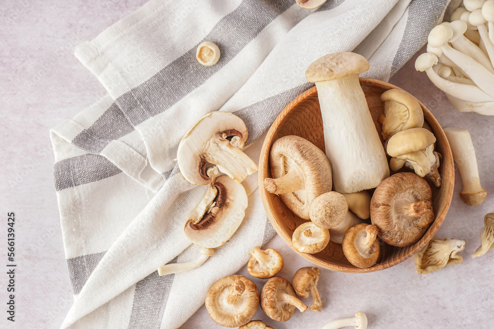 Wooden bowl with fresh mushrooms on light background