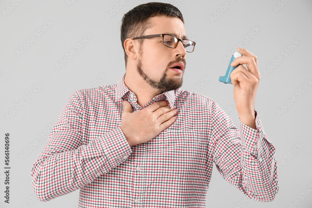Sick man with inhaler on light background