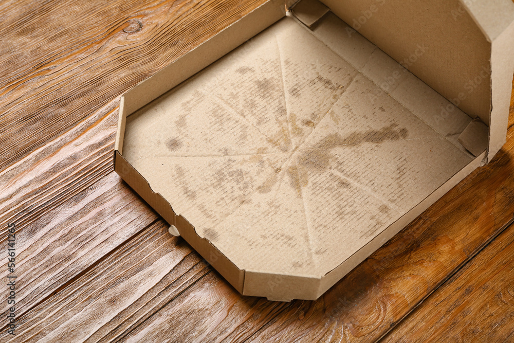 Empty greasy pizza box on wooden background