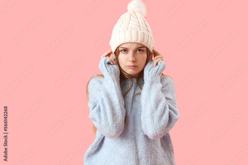Frozen young woman in warm hat and sweater on pink background