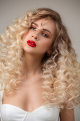 Wall Mural - Portrait of a beautiful blonde woman with red lipstick on her lips. Curly blond long hair. Hairstyle