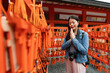 selective focus of pious asian Japanese girl surrounded by red wood plaques ema and making wish with hands together at Fushimi Inari Taisha shrine in Kyoto japan