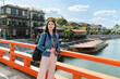 © PR Image Factory - smiling asian Japanese lady traveler looking at beautiful scenery on red uji bashi bridge over uji river with tourist boats on a sunny day in Kyoto japan