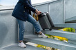 © PR Image Factory - cropped view of an unknown asian Japanese businessperson wearing suit jacket pulling bulky luggage down steps on city street